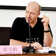 Caucasian man wearing black t-shirt seated at a table speaking into a thin microphone. Man is balding with a blond, trimmed,  mustache. Name placard reads Leopold Leeb.